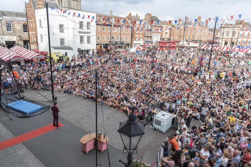 A big audience on a town square watching a person introducing a show act